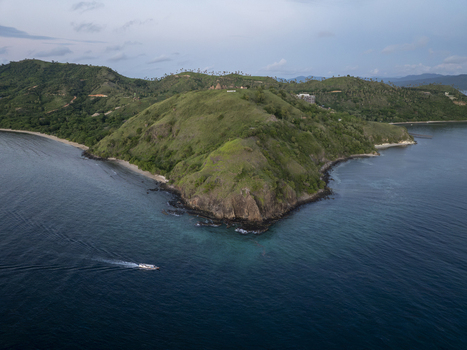 Aerial view of the lush green hills of Labuan Bajo meeting the turquoise waters of the sea with a small boat leaving a wake Komodo East Nusa Tenggara Indonesia. Aerial view of the lush green hills of Labuan Bajo meeting the turquoise waters of the sea with a small boat leaving a wake Komodo East Nusa Tenggara Indonesia.