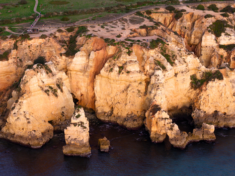 Aerial view of the golden limestone cliffs and sea caves at Ponta da Piedade with a wooden boardwalk and people walking along the coast in Lagos Faro Portugal.