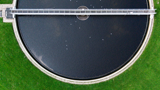 Aerial view of a circular wastewater treatment tank with a bridge structure and birds on the water surrounded by green grass in Warmenhuizen North Holland Netherlands. Aerial view of a circular wastewater treatment tank with a bridge structure and birds on the water surrounded by green grass in Warmenhuizen North Holland Netherlands.