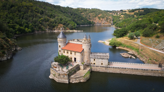 Aerial view of the Ch&acirc;teau de la Roche standing majestically in the glistening water surrounded by lush green hills Saint Priest la Roche Auvergne Rh&ocirc;ne Alpes France.