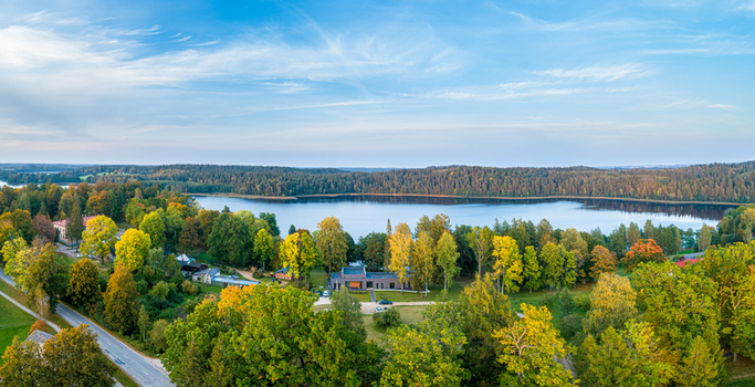 Aerial view of a serene lake surrounded by dense forests with vibrant autumn foliage under a clear blue sky in Latvia. Aerial view of a serene lake surrounded by dense forests with vibrant autumn foliage under a clear blue sky in Latvia.