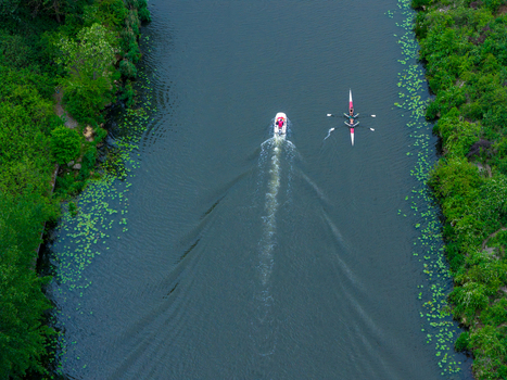 Poland 31 May 2026 Aerial view of a rowing boat and a motorboat navigating a river lined with lush green vegetation and water lilies.