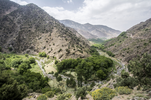 View of a lush green valley with a winding stream nestled between rugged mountain slopes under a cloudy sky in Tizi Oussem Marrakech Safi Morocco. View of a lush green valley with a winding stream nestled between rugged mountain slopes under a cloudy sky in Tizi Oussem Marrakech Safi Morocco.