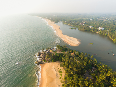Aerial view of a tropical coastline where a river meets the ocean featuring golden sand beaches lush palm groves and rocky shores in Galle Southern Province Sri Lanka.