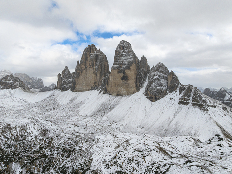 Aerial view of the majestic Tre Cime di Lavaredo peaks piercing the sky their rocky faces dusted with snow under a cloudy sky Dolomites Italy.