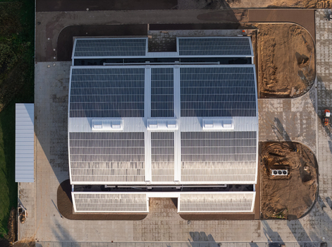 Aerial view of a large industrial building with extensive solar panel arrays on the roof surrounded by paved areas and construction grounds in Uckermark Brandenburg Germany. Aerial view of a large industrial building with extensive solar panel arrays on the roof surrounded by paved areas and construction grounds in Uckermark Brandenburg Germany.