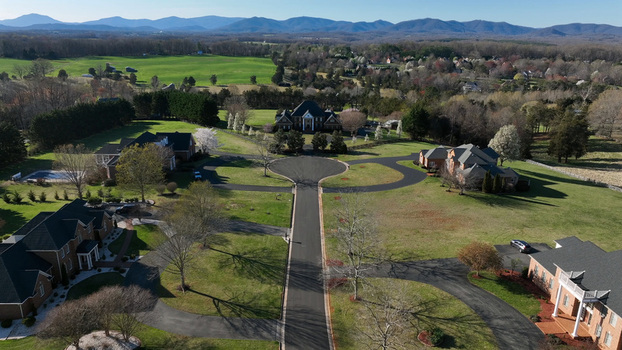 Aerial view of a suburban residential neighborhood with large houses manicured lawns winding driveways and distant mountains under a clear blue sky in Forest Virginia United States.