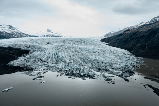 Aerial view of Vatnajokull glacier with its rugged ice formations and glacial lake surrounded by mountains in Iceland.