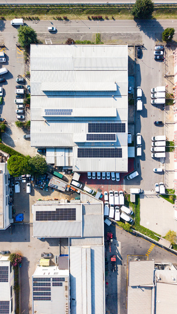 Aerial view of a transport company warehouse featuring solar panels on the roof and rows of white delivery vans parked in the loading area in Milan Lombardy Italy. Aerial view of a transport company warehouse featuring solar panels on the roof and rows of white delivery vans parked in the loading area in Milan Lombardy Italy.