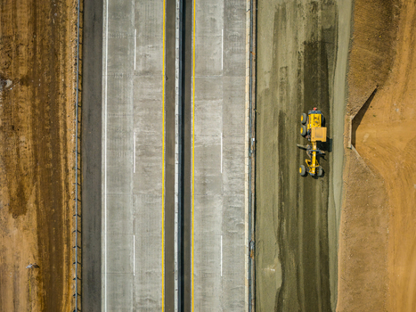 Aerial view of a yellow motor grader working on a new highway construction site with concrete lanes and surrounding earthworks Salatiga Central Java Indonesia.