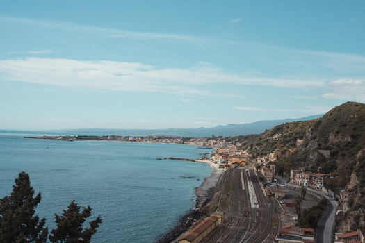 View of the coastline with a railway running alongside the sea buildings nestled between the tracks and the hills under a clear sky Taormina Sicily Italy. View of the coastline with a railway running alongside the sea buildings nestled between the tracks and the hills under a clear sky Taormina Sicily Italy.