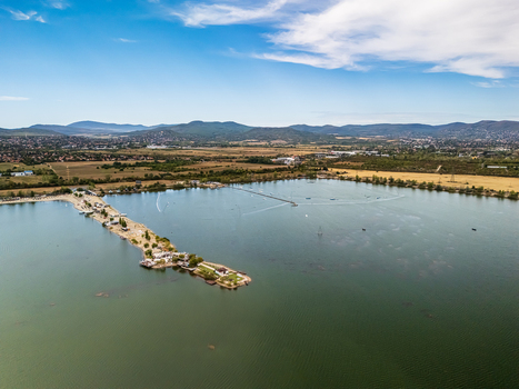 Aerial view of Lake Lupa s shoreline beach facilities and water sports course beside farmland and low hills in Budakalasz Hungary on a clear late summer day.