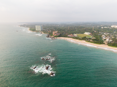 Aerial view of the tropical coastline featuring sandy beaches turquoise ocean waves and coastal buildings nestled among lush greenery in Galle Southern Province Sri Lanka.