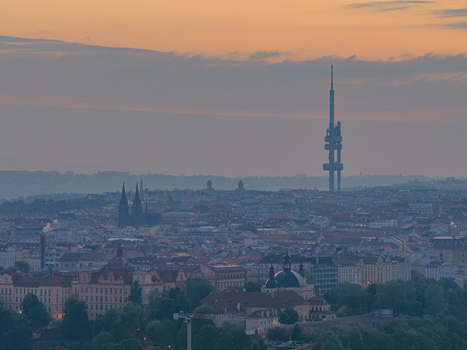 Aerial view of the Zizkov Television Tower rising above the historic skyline of Prague at sunset with soft golden light over the city rooftops Prague Prague Czechia.