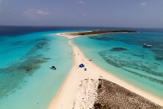 Aerial view of Los Roques archipelago featuring a narrow white sandbar surrounded by turquoise waters with small boats anchored nearby in Los Roques Dependencias Federales Venezuela. Aerial view of Los Roques archipelago featuring a narrow white sandbar surrounded by turquoise waters with small boats anchored nearby in Los Roques Dependencias Federales Venezuela.