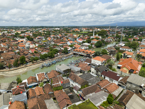 Aerial view of the Jepara Floating Fish Market where boats cluster reflecting the sky amid the town s terracotta roofs Jepara Central Java Indonesia.