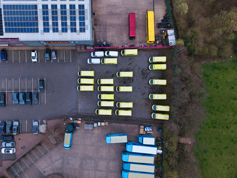 Aerial view of a fleet of yellow vans parked in a lot next to a warehouse contrasting with the red and blue vehicles and green grass Aylesbury United Kingdom. Aerial view of a fleet of yellow vans parked in a lot next to a warehouse contrasting with the red and blue vehicles and green grass Aylesbury United Kingdom.