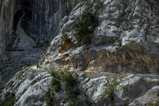 View of a narrow path carved into the rocky mountainside where tiny figures walk along the route in the Picos de Europa Picos de Europa Asturias Spain. View of a narrow path carved into the rocky mountainside where tiny figures walk along the route in the Picos de Europa Picos de Europa Asturias Spain.