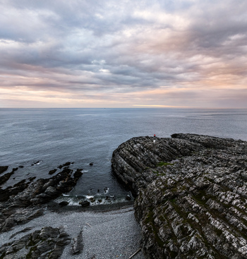 Aerial view of the Hamningberg lighthouse on a rugged rocky coastline overlooking the Barents Sea under a dramatic cloudy sky in Hamningberg Finnmark Norway. Aerial view of the Hamningberg lighthouse on a rugged rocky coastline overlooking the Barents Sea under a dramatic cloudy sky in Hamningberg Finnmark Norway.
