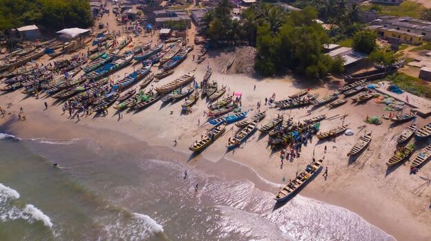 Aerial view of traditional wooden fishing boats resting on a sandy beach with local fishermen working near the shoreline in Ghana. Aerial view of traditional wooden fishing boats resting on a sandy beach with local fishermen working near the shoreline in Ghana.