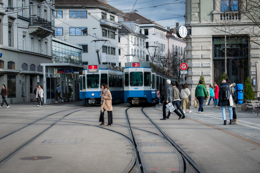 Zurich Switzerland 02 April 2023 View of trams gliding on tracks pedestrians crossing and buildings standing tall against a soft overcast sky near the National Museum Zurich. Zurich Switzerland 02 April 2023 View of trams gliding on tracks pedestrians crossing and buildings standing tall against a soft overcast sky near the National Museum Zurich.
