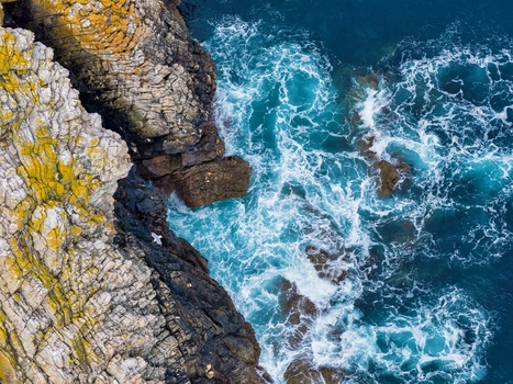 Aerial view of the rugged cliffs at Silence Beach Viewpoint with a seagull perched on rocks above turquoise waves in Cudillero Asturias Spain.