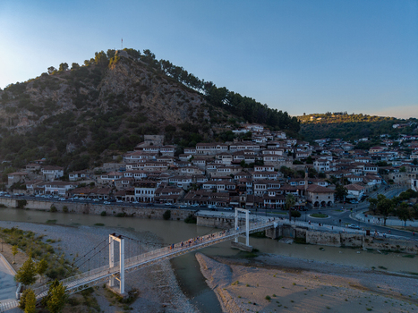 Aerial view of the historic town of Berat with its traditional white houses the Osum River and a pedestrian suspension bridge set against a hillside castle in Berat Berat County Albania.