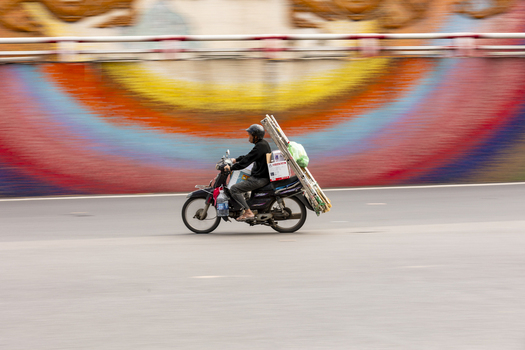 Hanoi Vietnam 11 November 2025 View of a motorcyclist carrying ladders and boxes along the colorful Ceramic Mosaic Mural in Hanoi Vietnam.