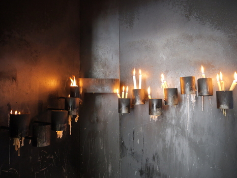 View of burning votive candles placed in metal holders against a dark soot stained wall in a church in Porto Portugal. View of burning votive candles placed in metal holders against a dark soot stained wall in a church in Porto Portugal.