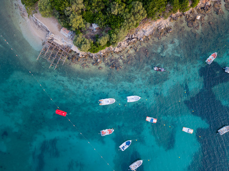 Aerial view of small boats anchored in turquoise waters along the rocky shoreline and lush green trees in Ksamil Vlore County Albania. Aerial view of small boats anchored in turquoise waters along the rocky shoreline and lush green trees in Ksamil Vlore County Albania.