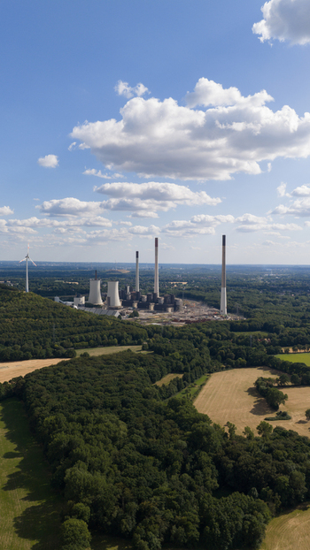 Aerial view of Scholven Power Station with tall chimneys and cooling towers amidst forests and fields under a blue sky in Gelsenkirchen Nordrhein Westfalen Germany.