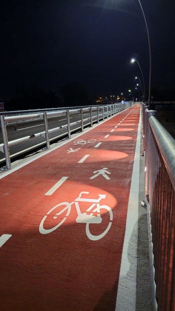 View of a red painted bicycle path on a bridge at night illuminated by streetlights with bicycle and pedestrian symbols in Macerata Marche Italy. View of a red painted bicycle path on a bridge at night illuminated by streetlights with bicycle and pedestrian symbols in Macerata Marche Italy.