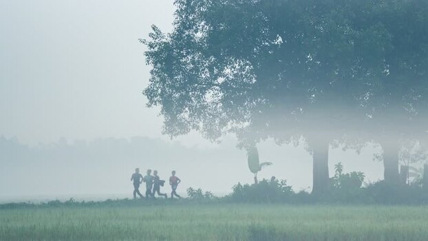 View of people running through a misty field in Bogura Bangladesh. View of people running through a misty field in Bogura Bangladesh.