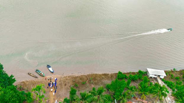 Aerial view of a small motorboat leaving a wake on the river near a group of people standing on the shore with moored boats in Minima Rivers Nigeria.