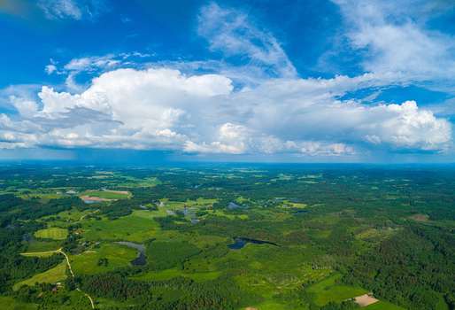 Aerial view of lush green forests fields and small ponds under a dramatic sky with large white clouds in Latvia. Aerial view of lush green forests fields and small ponds under a dramatic sky with large white clouds in Latvia.