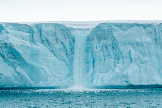 Svalbard and Jan Mayen 26 July 2025 View of a massive blue glacier wall with a meltwater waterfall cascading into the arctic sea under an overcast sky. Svalbard and Jan Mayen 26 July 2025 View of a massive blue glacier wall with a meltwater waterfall cascading into the arctic sea under an overcast sky.