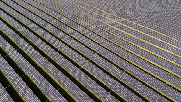 Aerial view of a large solar farm with rows of photovoltaic panels arranged in parallel lines across a field in Poland.