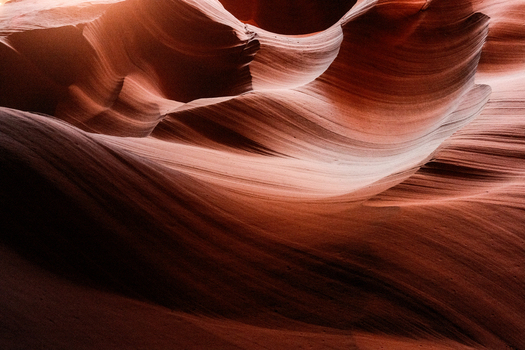 View of the smooth wavy sandstone walls of Antelope Canyon with soft light filtering through the slot canyon in Coconino County Arizona United States.