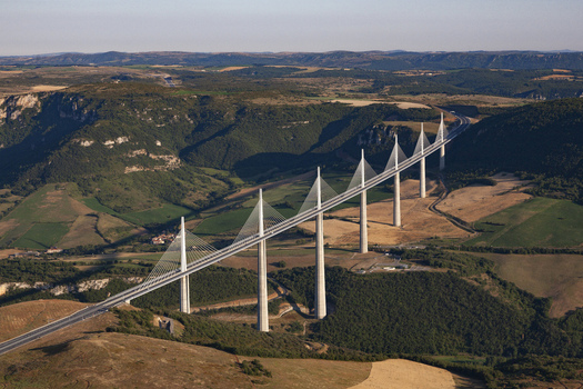 Aerial view of the Millau Viaduct piercing through the valley a symphony of concrete and cables against the backdrop of rolling hills Millau France. Aerial view of the Millau Viaduct piercing through the valley a symphony of concrete and cables against the backdrop of rolling hills Millau France.