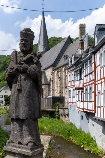 View of the stone statue of St. John of Nepomuk by the Elzbach river with half timbered houses and the parish church in Monreal Rhineland Palatinate Germany. View of the stone statue of St. John of Nepomuk by the Elzbach river with half timbered houses and the parish church in Monreal Rhineland Palatinate Germany.