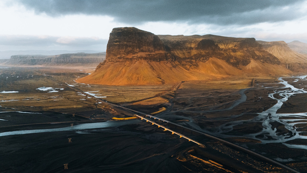 Aerial view of Lomagnupur mountain rising above a braided river system and a long bridge under a moody sky Skaftarhreppur Iceland.