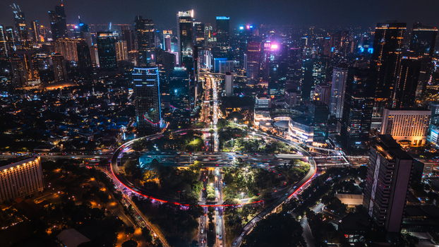 Aerial view of the illuminated Semanggi Interchange at night featuring circular traffic patterns glowing vehicle light trails and a dense skyline of modern skyscrapers in Jakarta Indonesia.