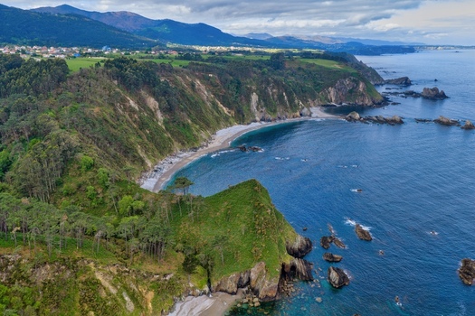 Aerial view of Silence Beach Viewpoint with rugged green cliffs a pebble beach and turquoise waters of the Cantabrian Sea in Cudillero Asturias Spain.