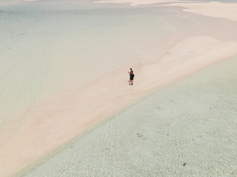 Aerial view of Pasir Timbul Mansuar sandbar in Raja Ampat with two people walking on the white sand surrounded by crystal clear turquoise water in Papua Barat Indonesia.