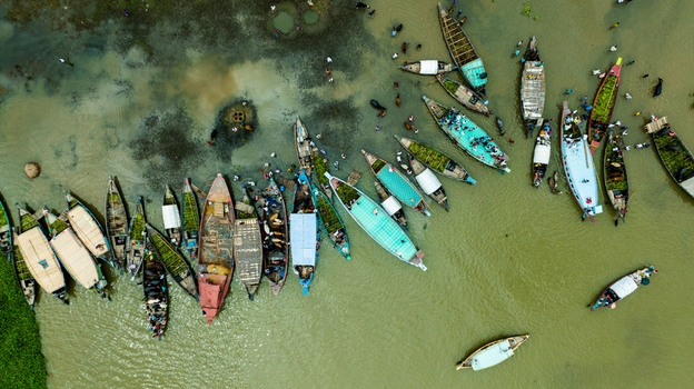 Aerial view of Baish Mowza Sarak Bazar with numerous wooden boats docked along the riverbank people loading goods and calm water in Nabinagar Chittagong Division Bangladesh. Aerial view of Baish Mowza Sarak Bazar with numerous wooden boats docked along the riverbank people loading goods and calm water in Nabinagar Chittagong Division Bangladesh.