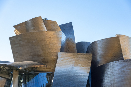 View of the Guggenheim Museum Bilbao featuring shimmering titanium panels and curved architectural forms under a clear blue sky Bilbao Euskadi Spain. View of the Guggenheim Museum Bilbao featuring shimmering titanium panels and curved architectural forms under a clear blue sky Bilbao Euskadi Spain.