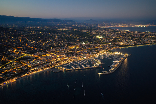 Aerial view of the illuminated harbor and coastline at night featuring docked yachts and city lights along the Mediterranean Sea in Antibes Provence Alpes Cote d Azur France. Aerial view of the illuminated harbor and coastline at night featuring docked yachts and city lights along the Mediterranean Sea in Antibes Provence Alpes Cote d Azur France.