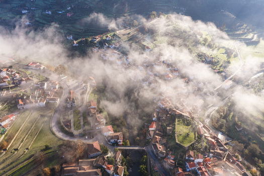 Aerial view of the historic village of Avo shrouded in morning mist with red roofed houses and terraced hillsides in Oliveira do Hospital Coimbra District Portugal.