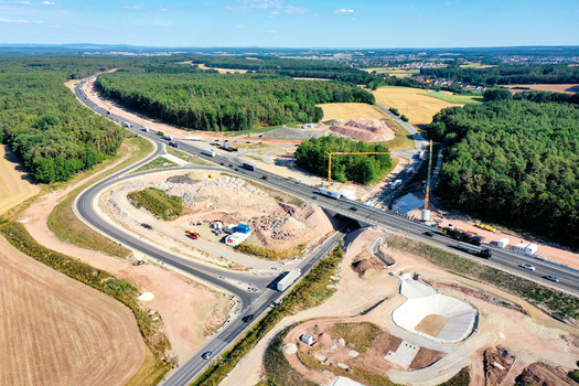 Aerial view of the A73 highway construction site with cranes heavy machinery and trucks passing through a forested landscape in Nurnberg Bayern Germany. Aerial view of the A73 highway construction site with cranes heavy machinery and trucks passing through a forested landscape in Nurnberg Bayern Germany.