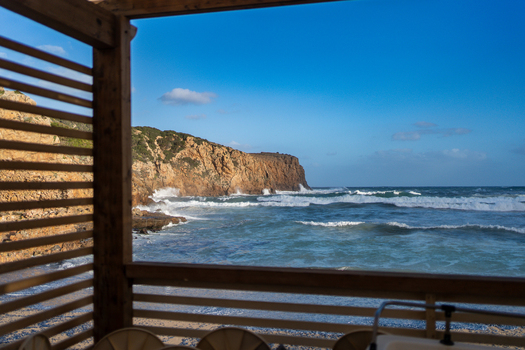 View of Spiaggia di Cala Domestica with waves crashing against the rugged cliffs under a clear blue sky in Provincia del Sulcis Iglesiente Sardegna Italy. View of Spiaggia di Cala Domestica with waves crashing against the rugged cliffs under a clear blue sky in Provincia del Sulcis Iglesiente Sardegna Italy.